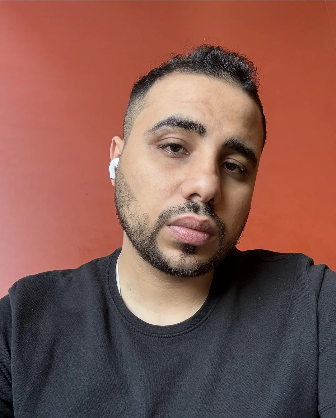 Samer Samir, AI engineer, portrait photo in a black t-shirt against an orange wall